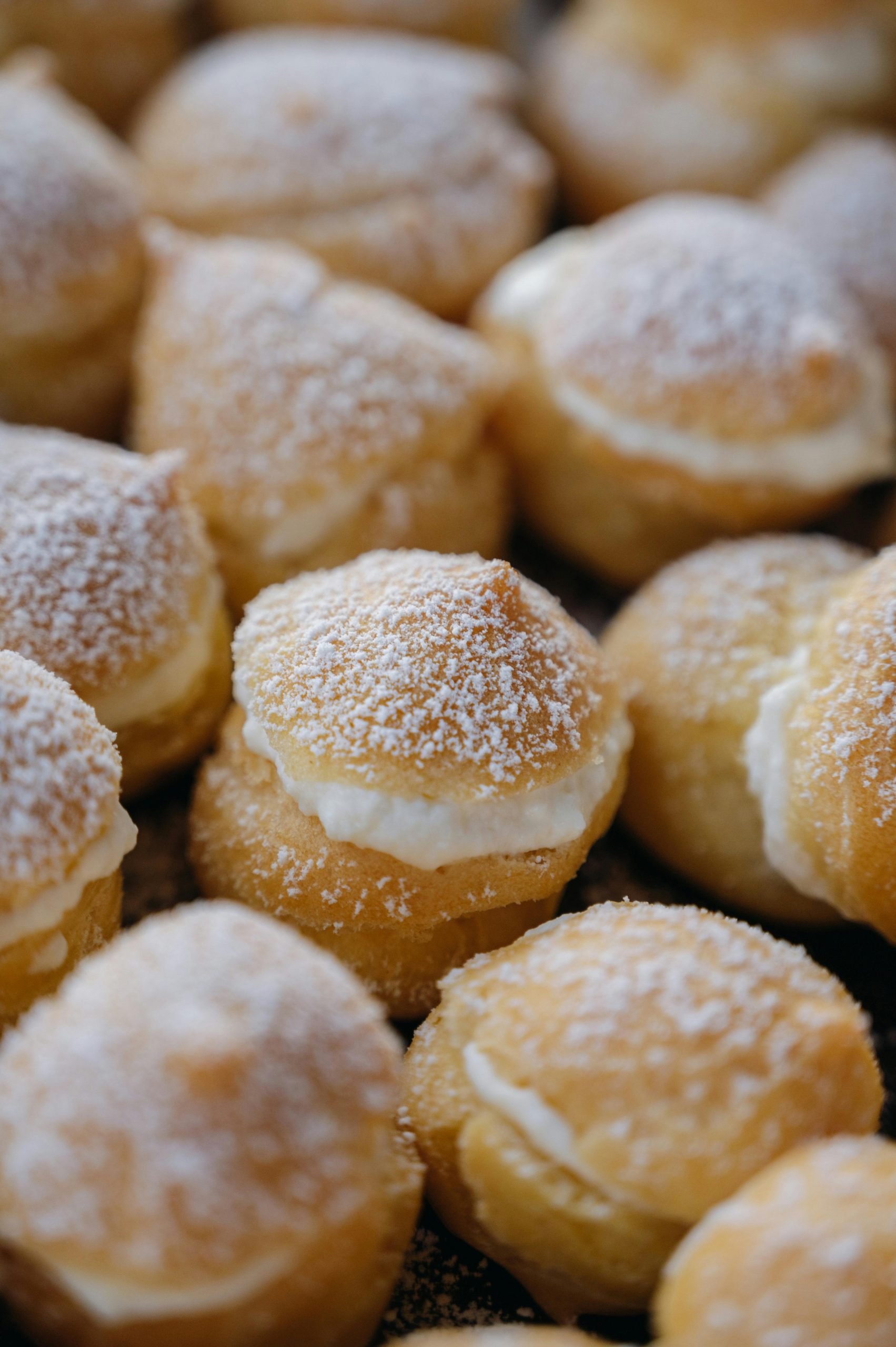 Close-up of cream-filled pastries topped with powdered sugar, shot indoors for a tempting dessert presentation.