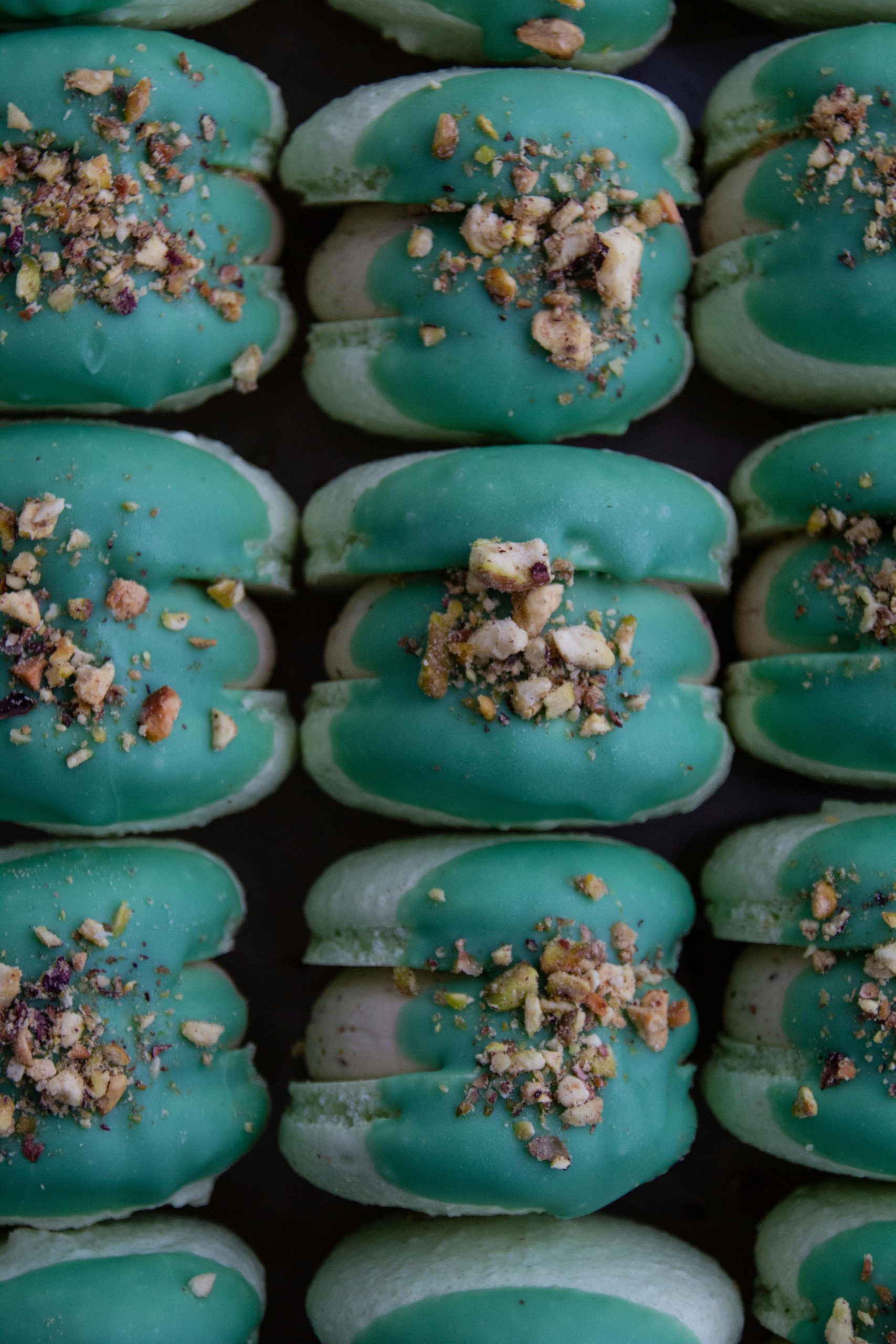 Delicious homemade macarons topped with nuts, showcasing vibrant green icing.